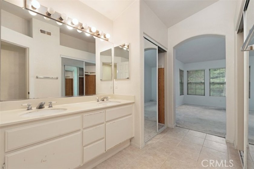 Reverse angle of master bathroom, showing dual sinks and dual closets with mirrored doors.