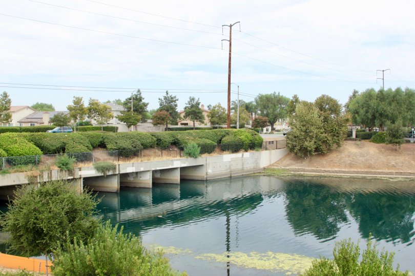 Overcast sky. Water is clear with little vegetation. The cars are passing over the bridge. Typical quiet day in Moreno Valley.