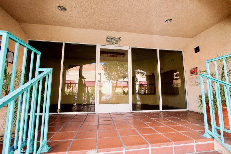 The glass front door to Villa Del Obispo with a clay tile floor and blue railing