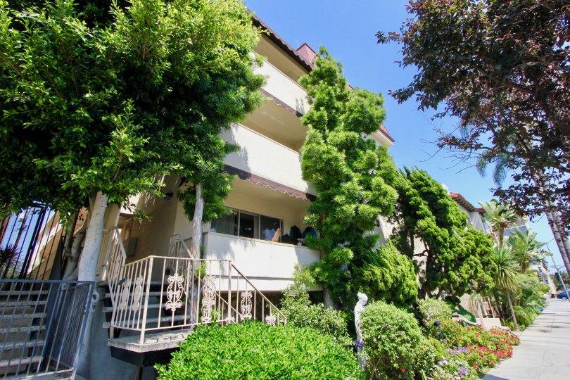 Three storey apartment building with balconies on each floor, vegetation in the front and a small statue.