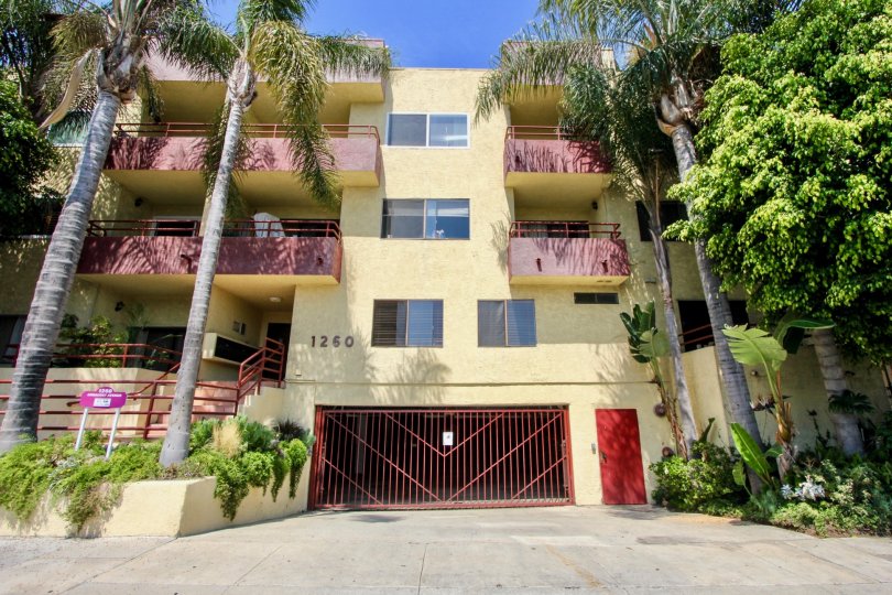 Apartment complex with palm trees and nice gardens and red garage fence underground garage balconies on building