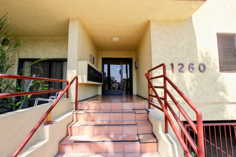 The entryway of an apartment building in the Brentwood Villas with stairs with red rails and the building's address