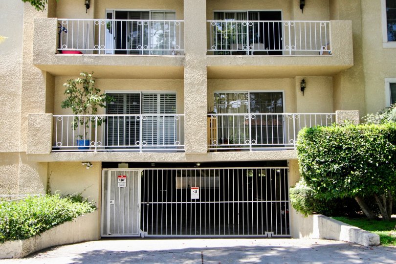 Front exterior view on a sunny day with bushes, balconies, and garage gate at Westwood Bentley in West LA, California