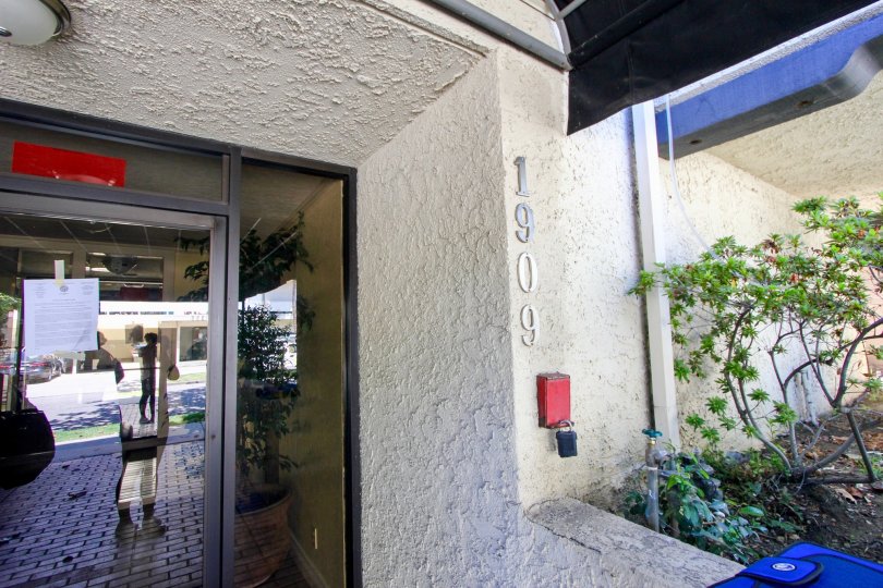 A white building in the Glendon Terrace II neighborhood with a glass front door and green plants