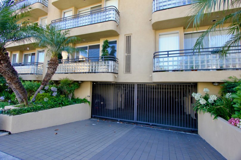 A tan multi-family housing facility with glass balcony railings and a gated parking garage in the Manning Plaza community of Westwood, California