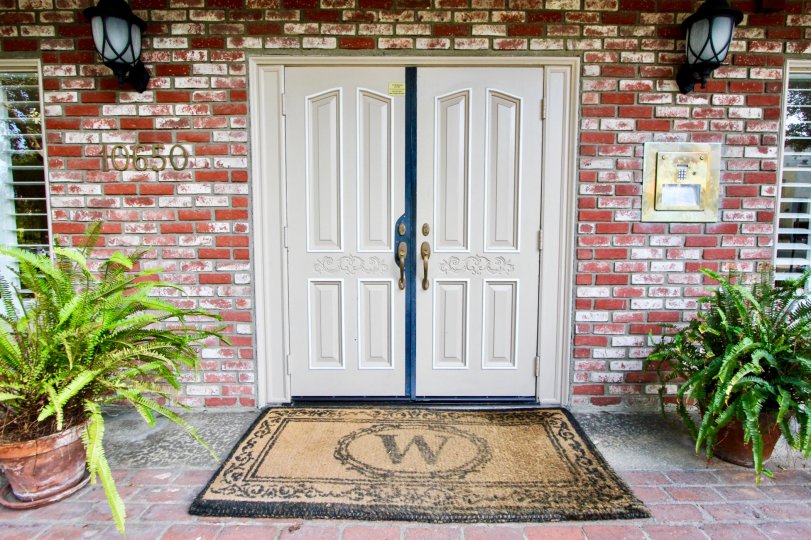 A white door on a brick building with blue trim on the door. There is a large mat outside the door with a 'W' on it.