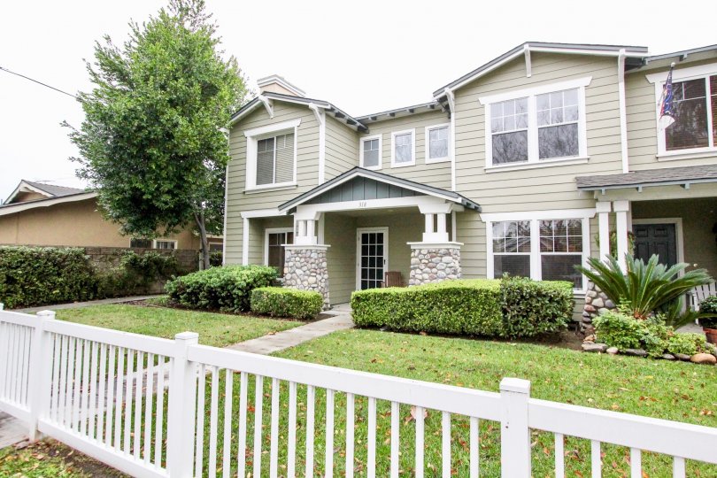 A large green front yard of a row of townhouses with a white vinyl picket fence out front.