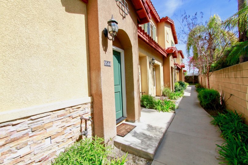 Sidewalk leading to entrances of townhomes. Greenery lines the walkway doors are enhanced with an entry light, address numbers, and bright colored doors.
