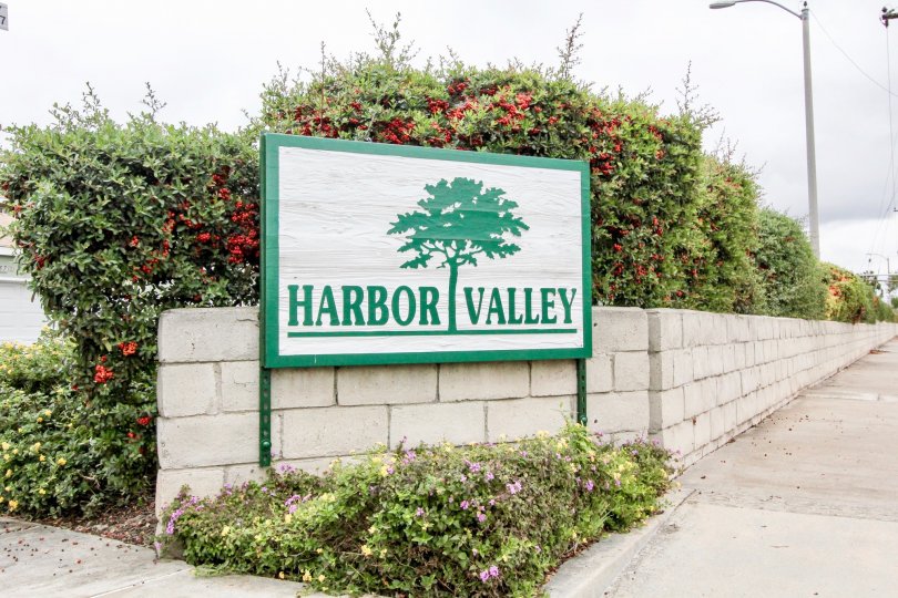 Entrance sign with green bushes with red in them showing the community name Harbor Valley.