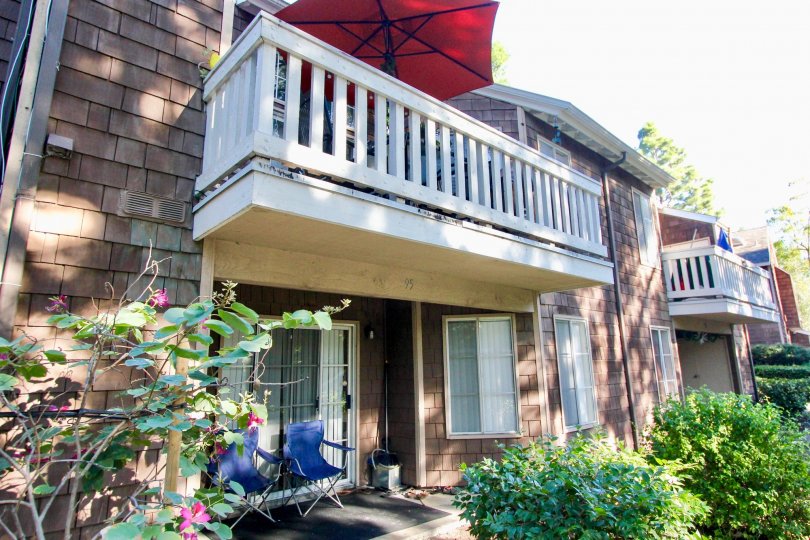 THIS VIEWS THE FRONT OF THE HOME WHICH HAS THE PLANTS, TWO CHAIRS, AND THE UMBRELLA IN THE PALCONY WHICH IS IN THE COMMUNITY OF LAKE GROVE