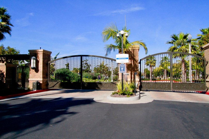 The front portion of the building in the Pacific Shores with big gates and palm trees, shrubs and camera.