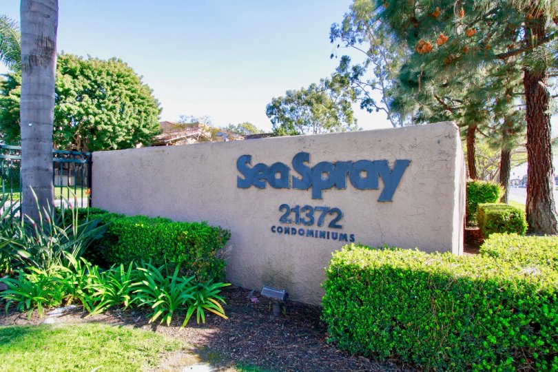 The entry sign at Sea Spray community located in Hunting Beach, CA. Surrounded by shrubs and a few trees