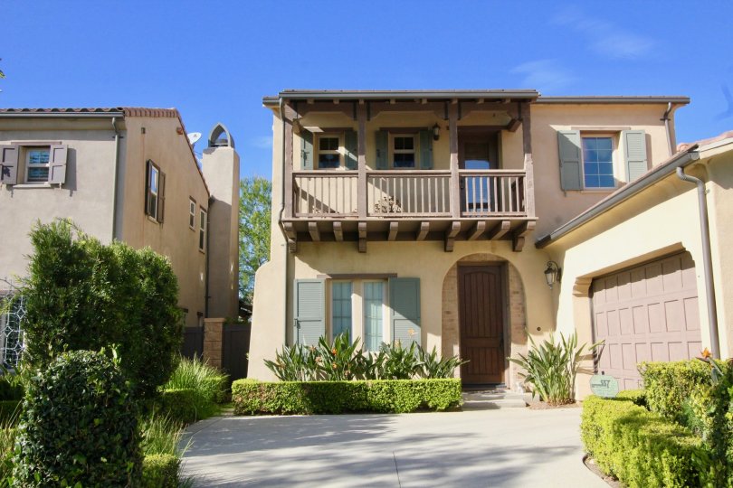 a tan home with a large balcony, garage, and arched entryway in Los Arboles