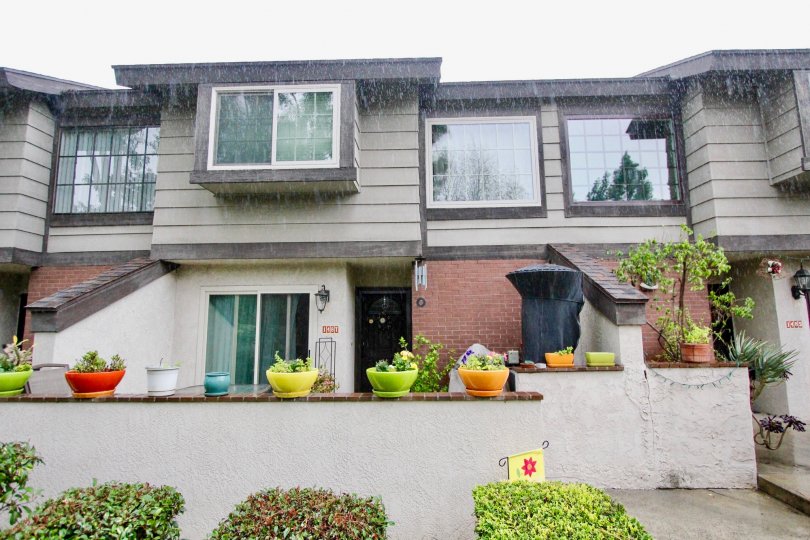a rainny day in the La Habra Woods Townhomes with a house that has small coloured flower pots in front and entrance door in the centre