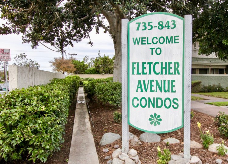 A white and green sign to the Fletcher Avenue condos surrounded with rocks