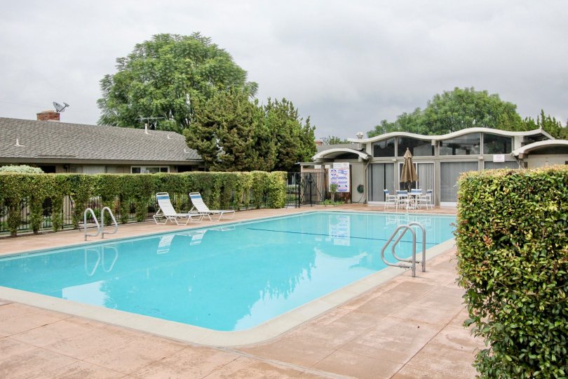 View of gated pool in Treehaven in Tustin, California. Lounge chairs and tables with umbrellas adorn the area.