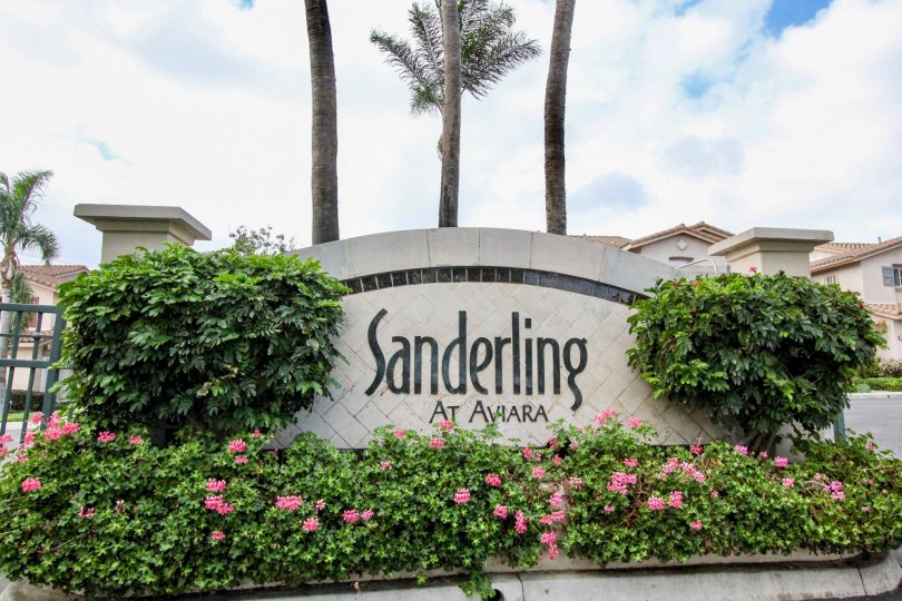 The welcome sign for Sanderling, surrounded by green bushes and budding pink flowers.