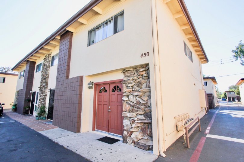 Holiday Gardens in Chula Vista, California. A cream-colored, two-story building sits under a bright blue sky. There is an entrance with closed red doors. Few cars are parked here.
