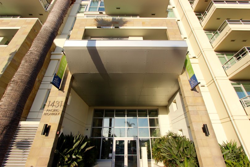 Sidewalk camera view angled up of the Brezza Condos Downtown San Diego California landescapeat front door of small palms