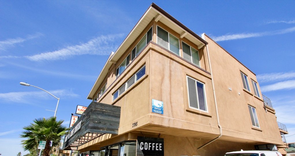 The exterior of a corner stucco building in Bay View Villas with a coffee shop in the first floor.