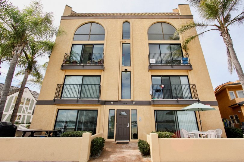 A four-story beige apartment building with palm trees on both sides and a front patio area in the Casa Bahia community of Mission Beach, CA