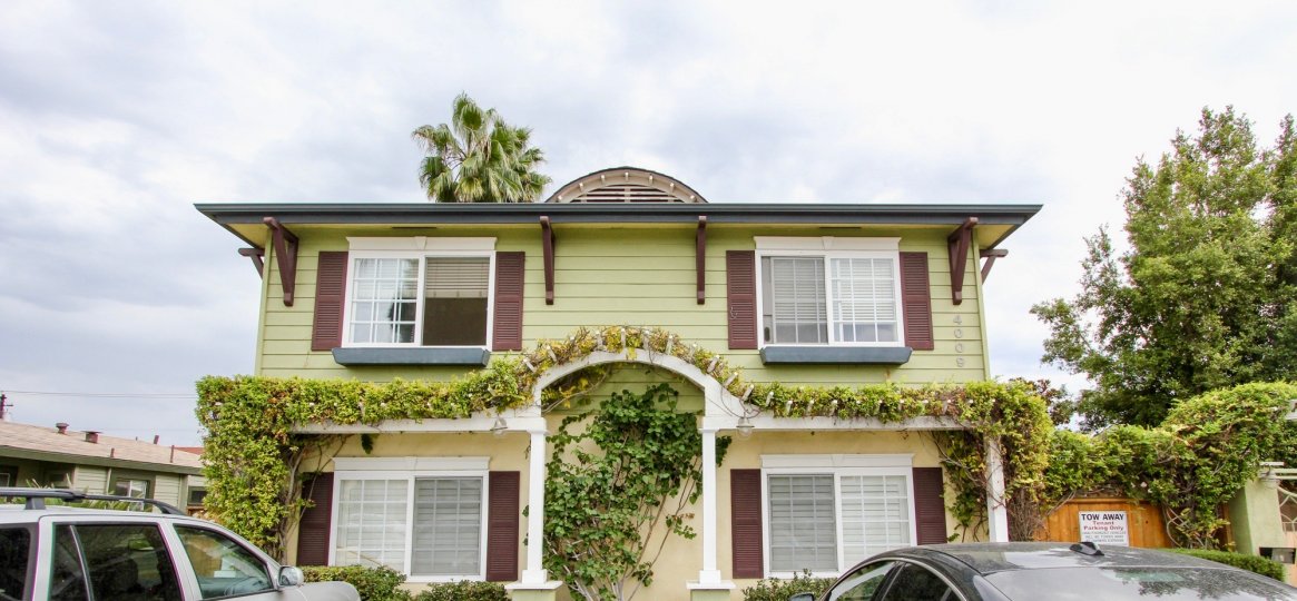A residence in Magnolia Walk, North Park, California with pastel green siding, brown accents, arched trellis with foliage over front entrance