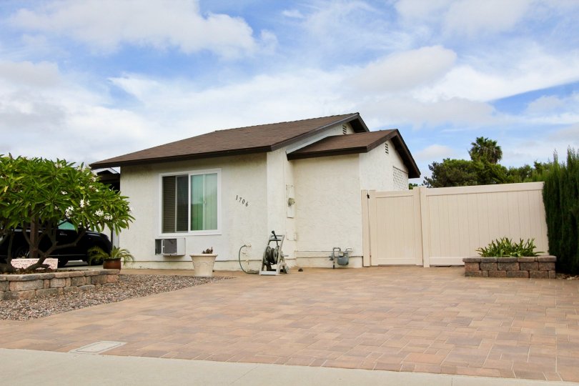 A white house front picture taken from street view. House located in Oceanside, California with a brick driveway and blue cloudy sky in the background.