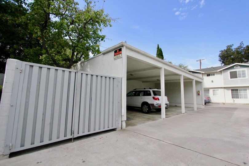A white car is parked in a carport near a car pakred in the open in front of a white and light gray apartment building in the Lamar Townhomes community in Spring Valley California