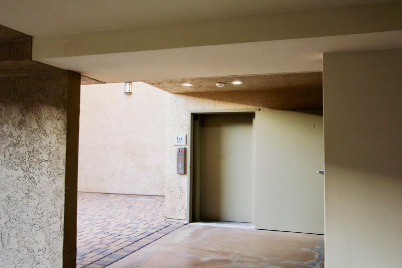 Inside of a bulding with a door, elevator, and wide open area to the left, located in Villa Vicenza, University City, California.